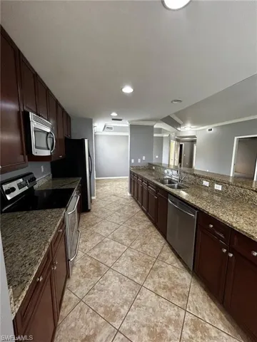 Kitchen with appliances with stainless steel finishes, a sink, light tile patterned flooring, stone countertops, and dark brown cabinetry