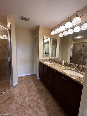 Bathroom featuring a shower stall, baseboards, double vanity, and tile patterned floors