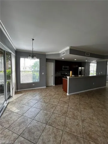 Kitchen with crown molding, appliances with stainless steel finishes, a chandelier, tile patterned flooring, and baseboards