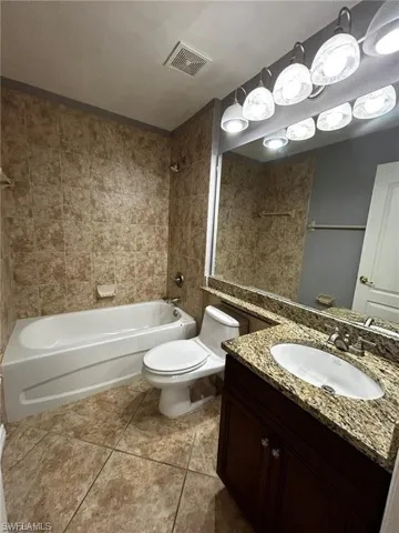 Bathroom featuring washtub / shower combination, tile patterned flooring, toilet, and vanity