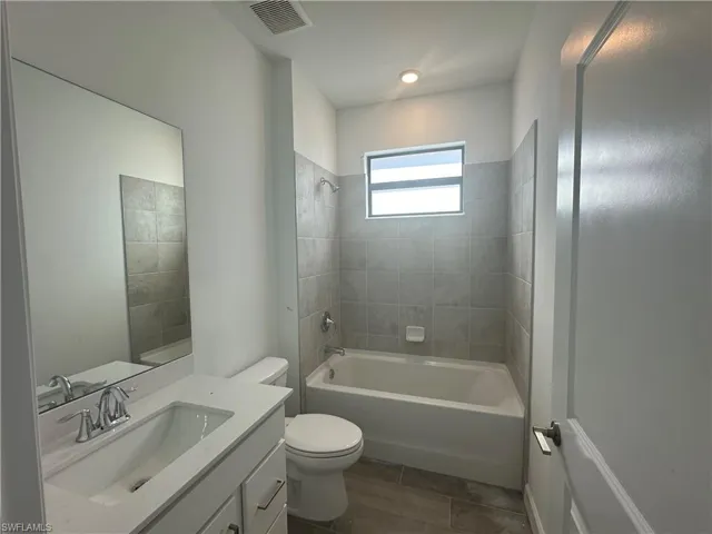 Full bathroom with tile floors, tiled shower / bath, toilet, and vanity
