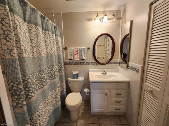 Full bath with a closet, vanity, tile walls, a shower with curtain, and tile patterned flooring