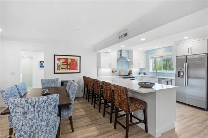 Kitchen with wall chimney range hood, white cabinetry, light hardwood / wood-style flooring, and appliances with stainless steel finishes
