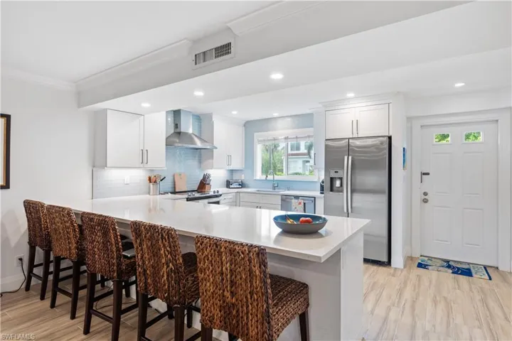 Kitchen featuring stainless steel appliances, white cabinetry, a breakfast bar, kitchen peninsula, and wall chimney exhaust hood