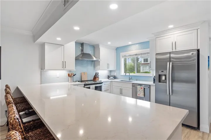 Kitchen with stainless steel appliances, wall chimney exhaust hood, kitchen peninsula, and light stone counters