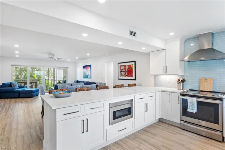 Kitchen featuring stainless steel appliances, light hardwood / wood-style floors, kitchen peninsula, white cabinets, and wall chimney range hood