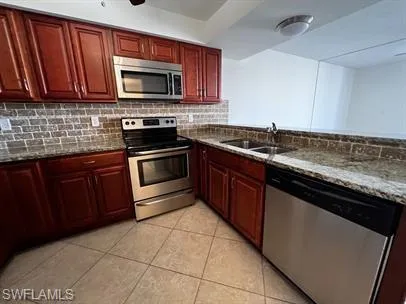 Kitchen with stainless steel appliances, reddish brown cabinets, dark stone countertops, and light tile patterned flooring
