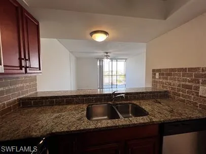Kitchen with backsplash, bold wood finish cabinets, dishwasher, dark stone counters, and ceiling fan