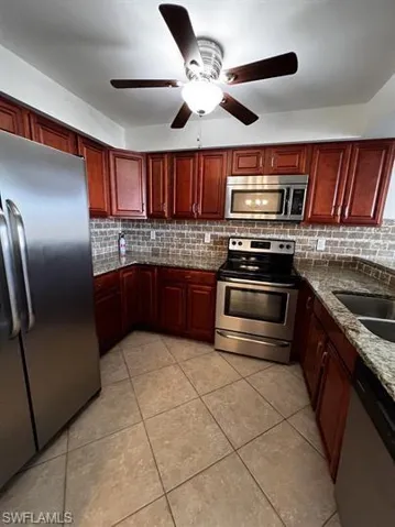 Kitchen featuring bold wood finish cabinetry, stainless steel appliances, dark stone countertops, a ceiling fan, and light tile patterned floors