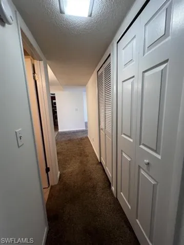 Hall with a textured ceiling and dark colored carpet