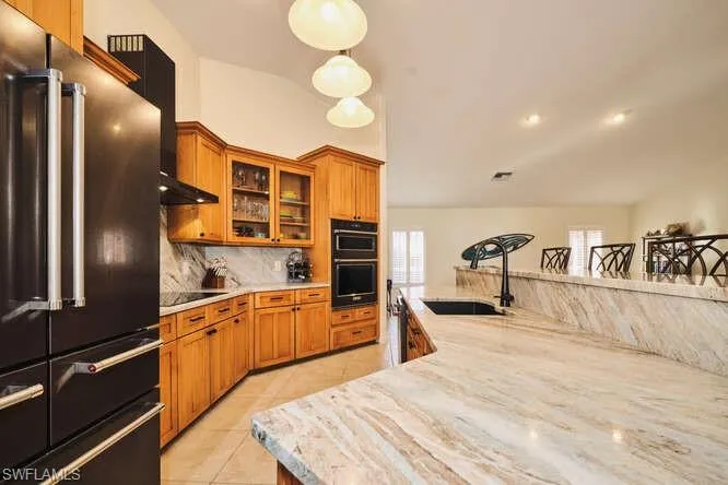 Kitchen featuring wood finish cabinets, black appliances, glass fronted cabinets, light stone counters, and light tile patterned floors