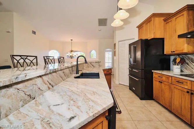 Kitchen featuring dishwasher, light stone counters, wood finish cabinets, a ceiling fan, and light tile patterned floors