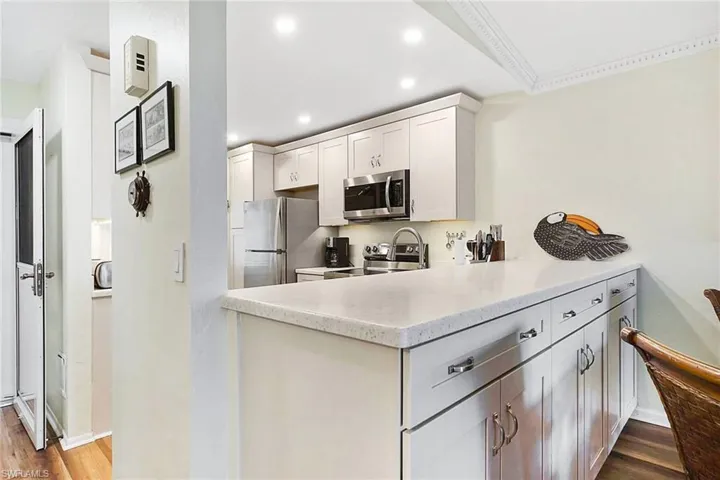 Kitchen featuring dark wood finished floors, light stone countertops, appliances with stainless steel finishes, recessed lighting, and white cabinetry