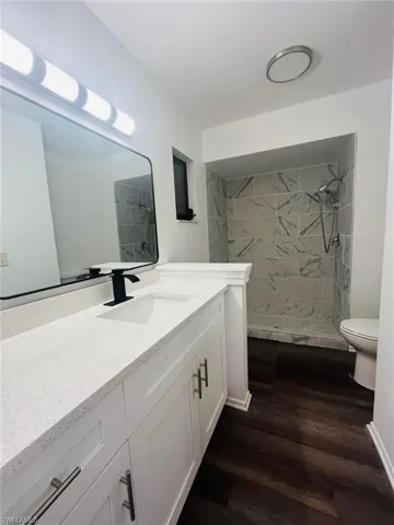 Spacious bathroom featuring a white vanity with an integrated sink and matte black faucet, a large rectangular mirror, and a tiled shower with a dark wood-finish floor