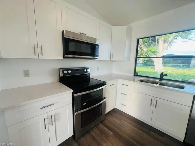 Modern kitchen featuring white cabinetry with brushed nickel hardware, light-toned countertops, wood-finish flooring, and stainless steel appliances