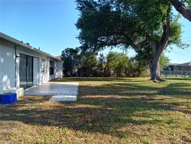 Expansive backyard featuring a large tree, a tiled patio, and sliding glass doors