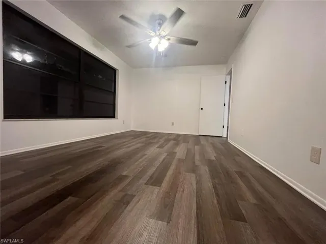 Spacious room featuring wood-finish flooring, white walls, and a ceiling fan with integrated lighting