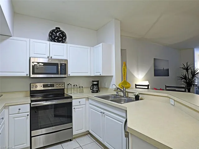 Kitchen featuring stainless steel appliances, light countertops, light tile patterned flooring, and white cabinets