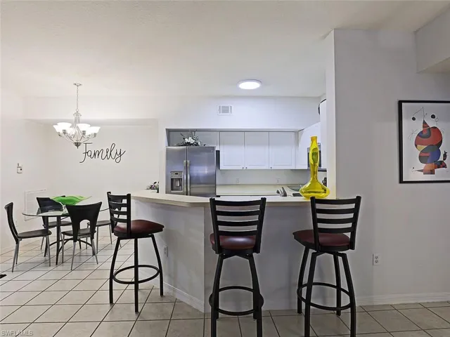 Kitchen featuring stainless steel refrigerator with ice dispenser, a chandelier, light tile patterned floors, white cabinets, and a peninsula