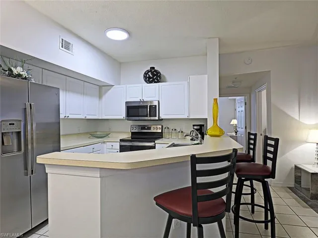Kitchen with stainless steel appliances, a peninsula, light tile patterned floors, and light countertops
