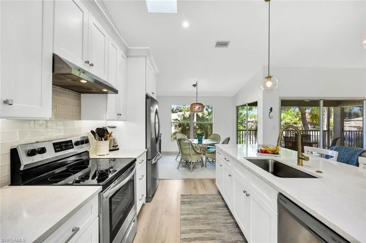 Kitchen featuring stainless steel appliances, white cabinets, pendant lighting, and lofted ceiling