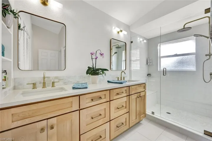 Full bath with double vanity, a shower stall, light tile patterned floors, and decorative backsplash