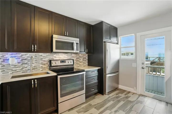 Kitchen featuring appliances with stainless steel finishes, backsplash, light countertops, and dark brown cabinetry- Virtually Enhanced