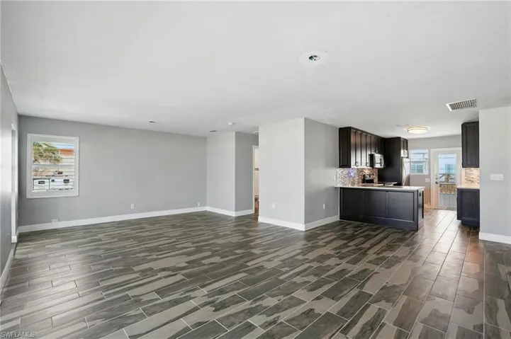Kitchen featuring open floor plan, wood finish floors, light countertops, stainless steel microwave, and a peninsula- Virtually Enhanced