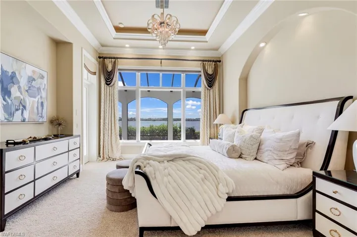 Bedroom with a tray ceiling, crown molding, a chandelier, and light carpet
