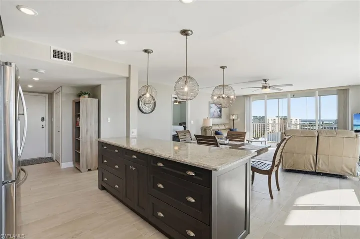 Kitchen with freestanding refrigerator, light stone counters, suspended lighting, open floor plan, and a kitchen island - Virtually Edited Image