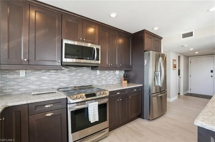 Kitchen featuring dark wood finish cabinetry, stainless steel appliances, light stone countertops, light wood-type flooring, and recessed lighting - Virtually Edited Image