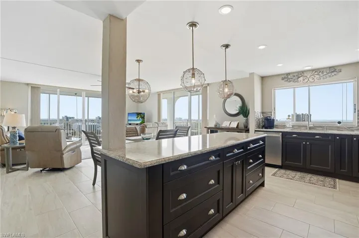 Kitchen featuring open floor plan, light stone counters, a kitchen island, and plenty of natural light - Virtually Edited Image