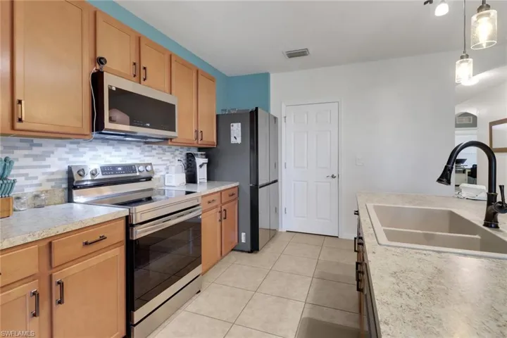 Kitchen with appliances with stainless steel finishes, decorative light fixtures, decorative backsplash, sink, and light tile patterned flooring