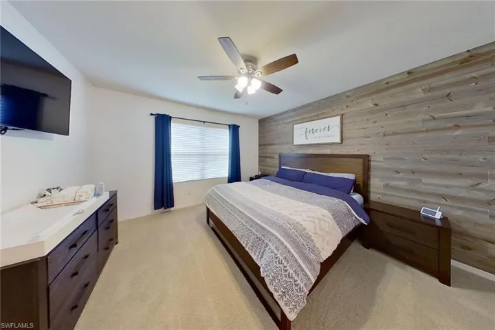 Carpeted bedroom featuring ceiling fan and wood walls