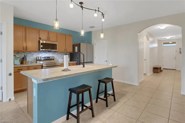 Kitchen with backsplash, appliances with stainless steel finishes, an island with sink, and pendant lighting