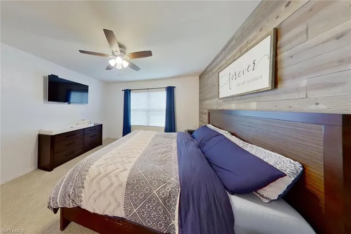 Bedroom featuring ceiling fan, light carpet, and wooden walls