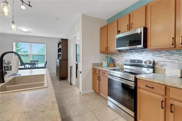 Kitchen featuring appliances with stainless steel finishes, decorative light fixtures, sink, backsplash, and light tile patterned floors