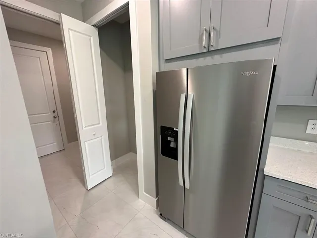Kitchen with gray cabinetry, stainless steel refrigerator with ice dispenser, light stone counters, and light tile patterned floors