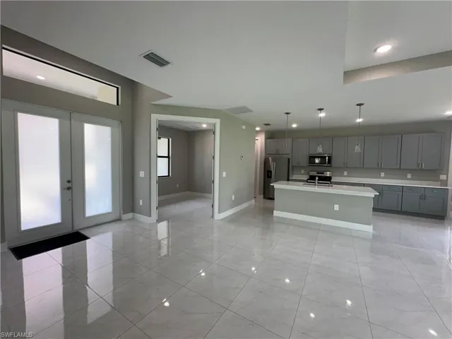Kitchen with appliances with stainless steel finishes, french doors, hanging light fixtures, light tile patterned floors, and an island with sink
