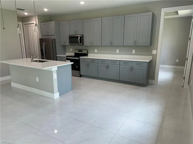 Kitchen with light tile patterned flooring, appliances with stainless steel finishes, a kitchen island with sink, gray cabinetry, and sink