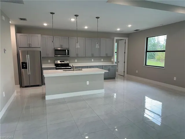 Kitchen featuring stainless steel appliances, light tile patterned floors, a center island with sink, and gray cabinets