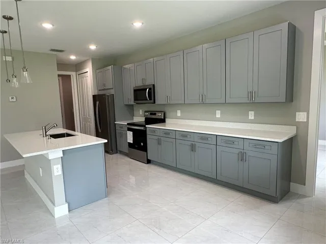 Kitchen with gray cabinetry, sink, stainless steel appliances, and pendant lighting