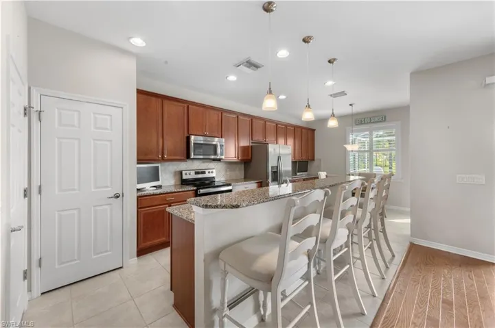Kitchen featuring appliances with stainless steel finishes, backsplash, a breakfast bar area, light stone counters, and brown cabinetry