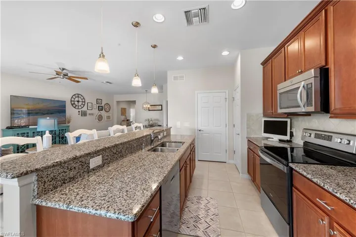 Kitchen featuring appliances with stainless steel finishes, open floor plan, a ceiling fan, an island with sink, and light stone counters