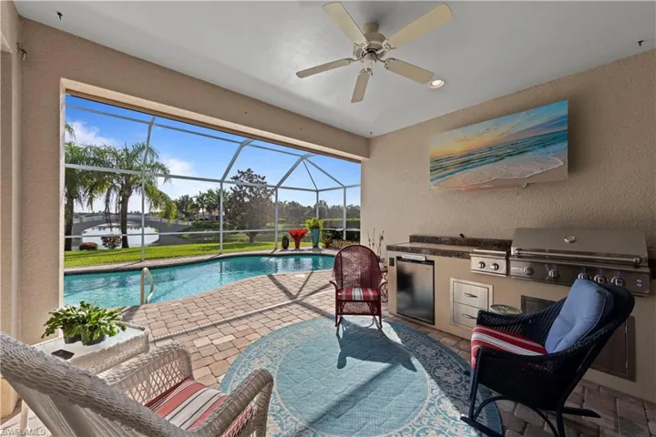 Swimming pool with an outdoor kitchen, a patio area, ceiling fan, and glass enclosure