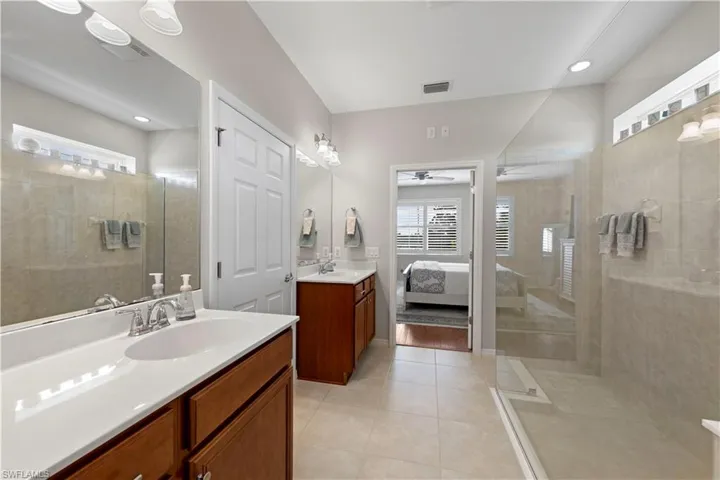 Ensuite bathroom with two vanities, walk in shower, tile patterned floors, and ceiling fan