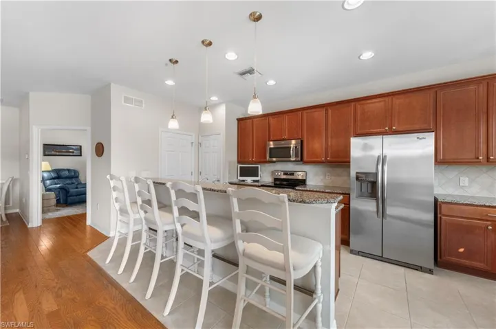 Kitchen featuring appliances with stainless steel finishes, light stone countertops, decorative backsplash, a kitchen bar, and a kitchen island