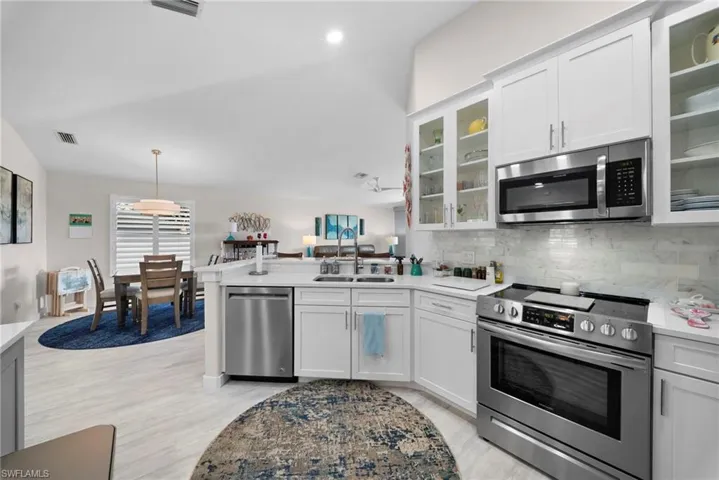 Kitchen featuring stainless steel appliances, a peninsula, white cabinetry, decorative backsplash, and glass insert cabinets