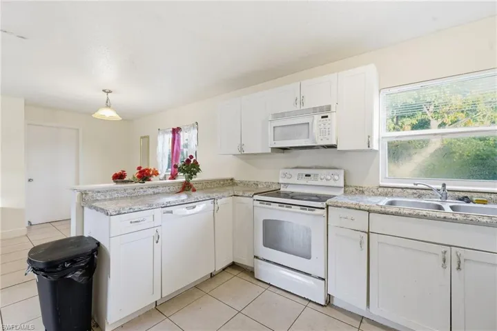 Kitchen with white appliances, white cabinets, a peninsula, light countertops, and decorative light fixtures