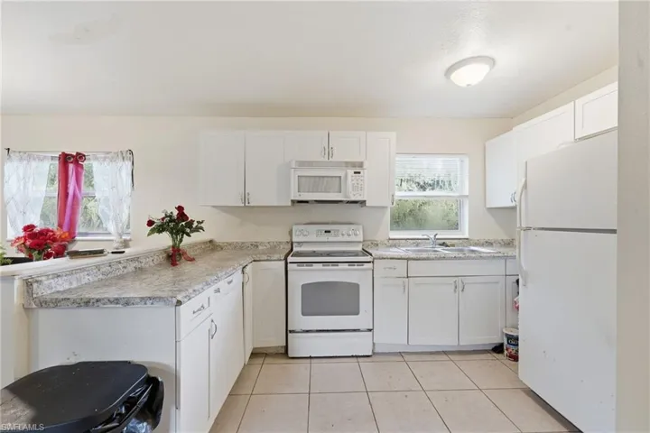 Kitchen with white appliances, white cabinetry, light countertops, light tile patterned floors, and a peninsula